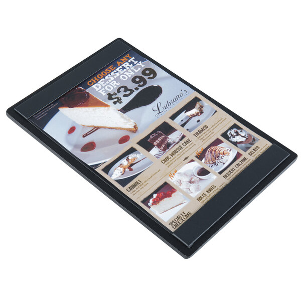 A Menu Solutions black wood menu board with top and bottom strips on a counter with a picture of a cake.
