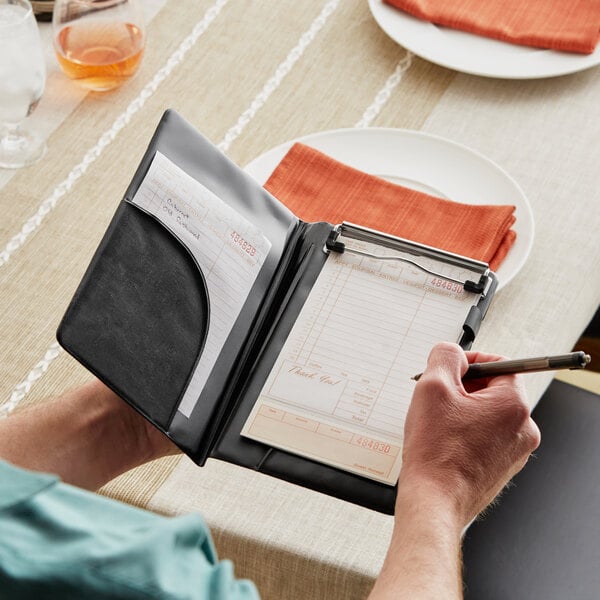 A man using a black vinyl server book with a wallet pocket and clip to hold a pen and notepad.