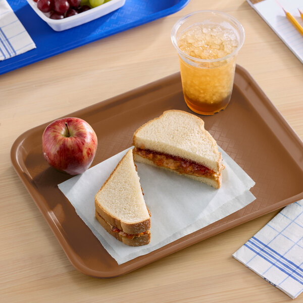 A brown plastic fast food tray holding a peanut butter and jelly sandwich, an apple, and a cup of iced beverage.