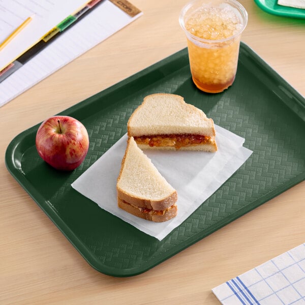 A forest green plastic fast food tray holding a sandwich, an apple, and a cup of iced drink.