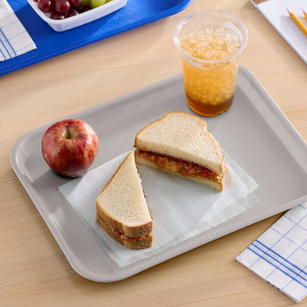 A gray plastic fast food tray holding a sandwich, an apple, and a cup of iced drink.