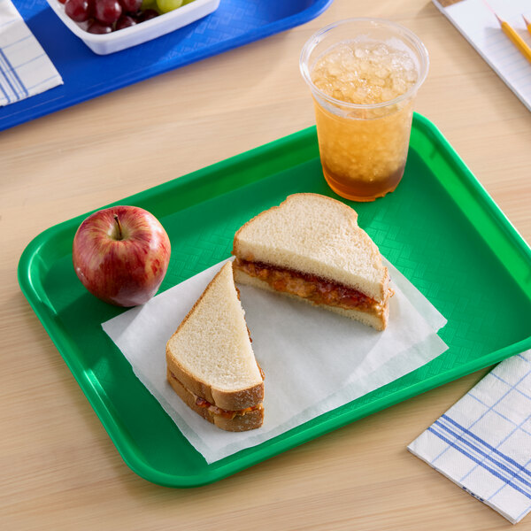 A green plastic fast food tray holding a peanut butter and jelly sandwich, an apple, and a cup of iced beverage.