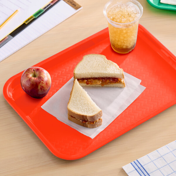 A bright orange plastic fast food tray holding a peanut butter and jelly sandwich, an apple, and a cup of iced drink.