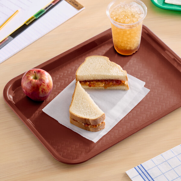 A burgundy plastic fast food tray holding a peanut butter and jelly sandwich, an apple, and a cup of iced drink.