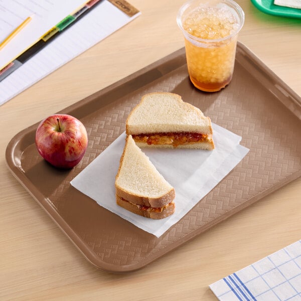 A brown plastic fast food tray holding a peanut butter and jelly sandwich, an apple, and a cup of iced drink.