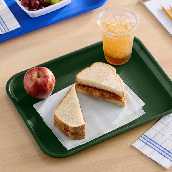 A green plastic fast food tray holding a sandwich, an apple, and a cup of iced beverage.