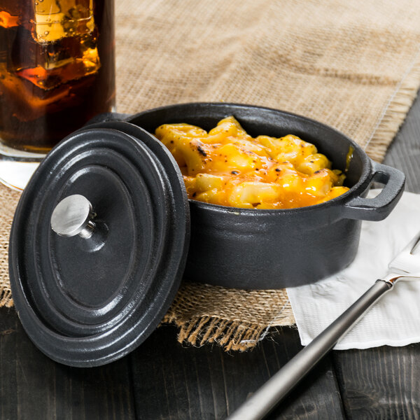 A black Libbey mini cast iron oval dutch oven with food in it and a lid on a table.