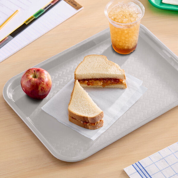 A gray plastic fast food tray holding a peanut butter and jelly sandwich, an apple, and a cup of iced drink.