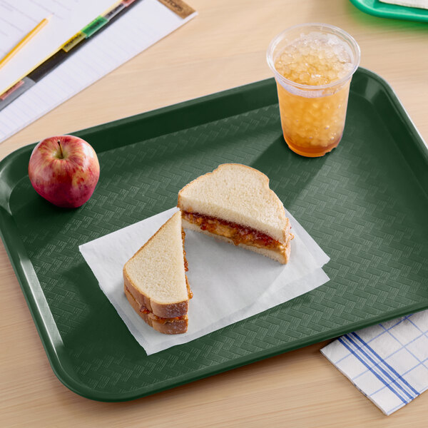 A forest green plastic fast food tray holding a sandwich, an apple, and a cup of iced drink.