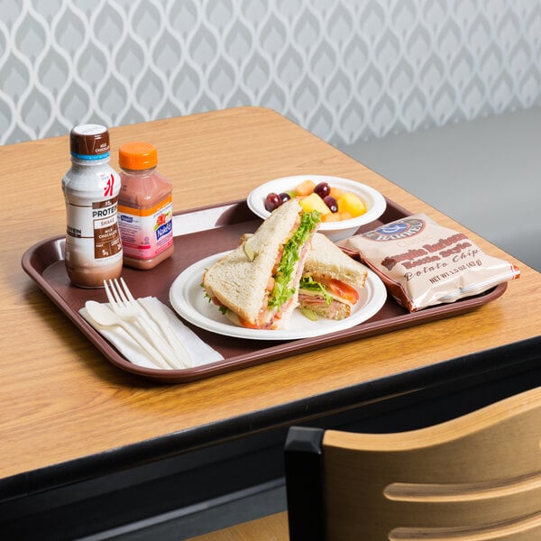 A burgundy plastic fast food tray with sandwiches, fruit, and drinks on it.