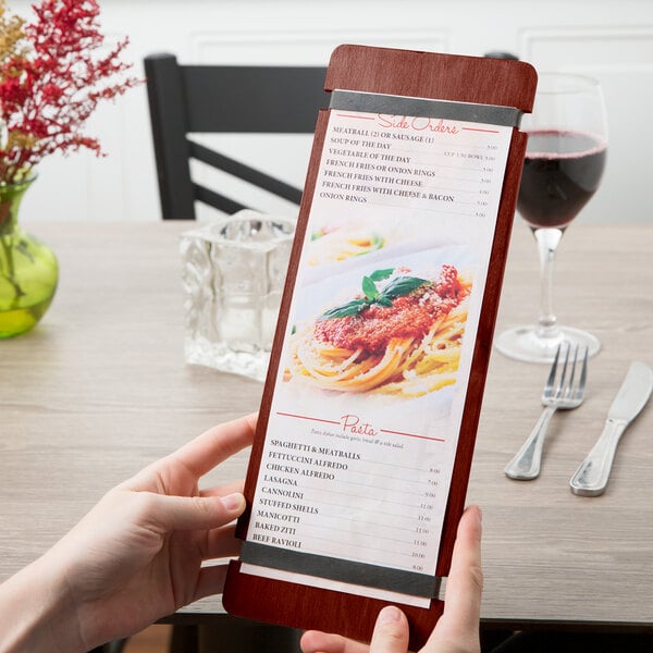 A person holding a mahogany wood menu board with rubber band straps on a table.