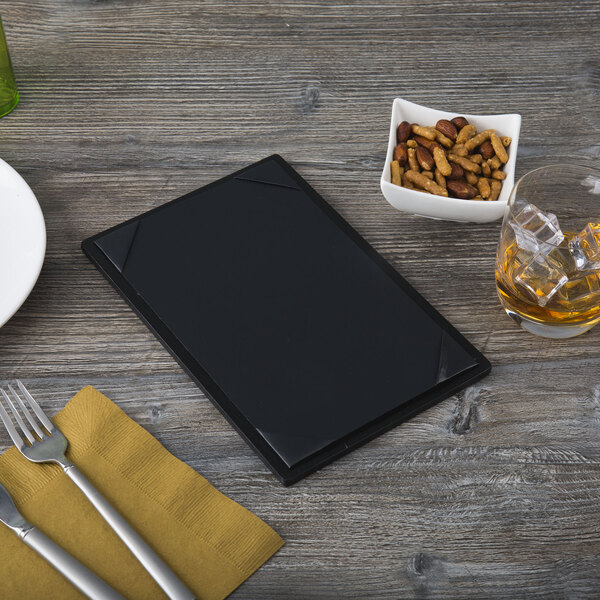 A black Menu Solutions wood menu board on a table with a plate, fork, and knife.