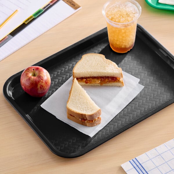 A black plastic fast food tray holding a peanut butter and jelly sandwich, an apple, and a cup of iced drink.