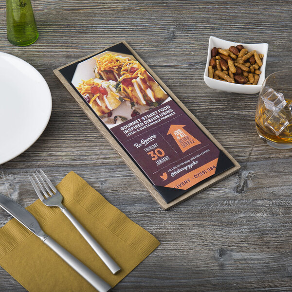 A customizable wood menu board with top and bottom strips on a table with a menu, fork, and knife.