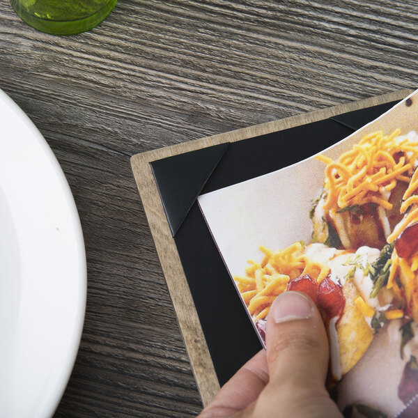A person holding a Menu Solutions wood menu board over a plate of food.