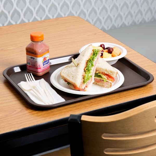 A sandwich and fruit on a Choice chocolate brown plastic fast food tray with a bottle of liquid.