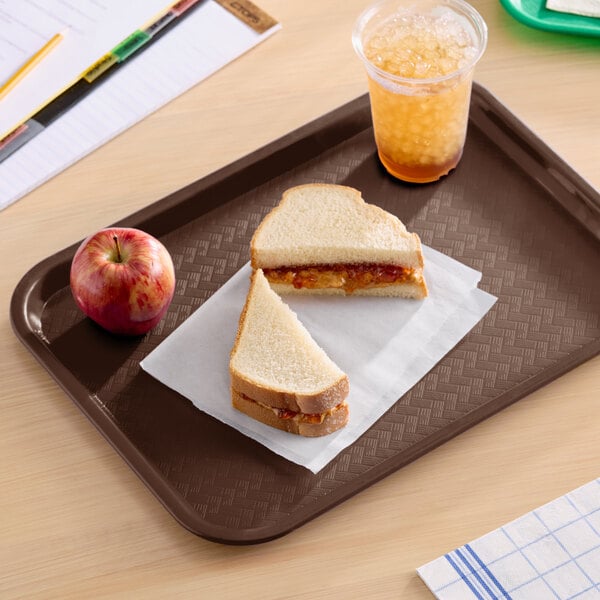 A chocolate brown plastic fast food tray holding a peanut butter and jelly sandwich, an apple, and a cup of iced drink.