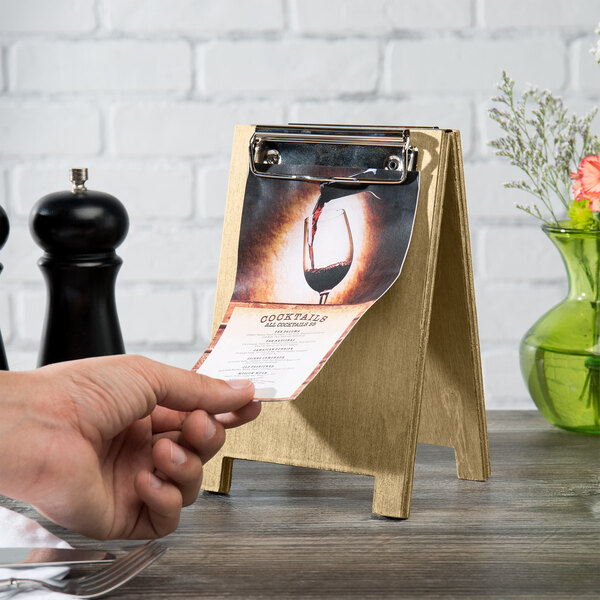 A hand using a Menu Solutions natural wood sandwich menu board tent with clip on a table.
