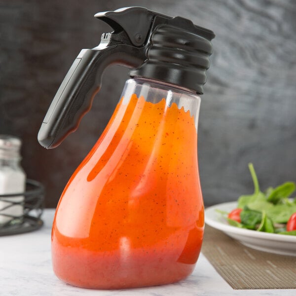 A Tablecraft Tritan dispenser bottle of orange sauce on a table next to a bowl of salad.