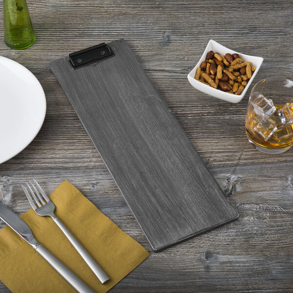 A customizable wood menu clip board on a table with a plate and a glass of whiskey.