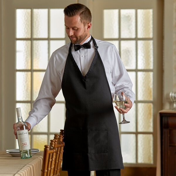 A man in a Choice black server tuxedo holding a glass of wine and a bottle.