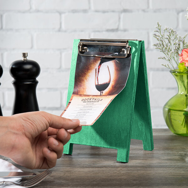 A hand holding a Menu Solutions washed teal wood sandwich menu board tent on a table.