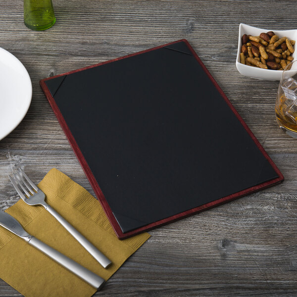 A mahogany wood menu board with silver picture corners on a table with a white plate, fork, and knife.