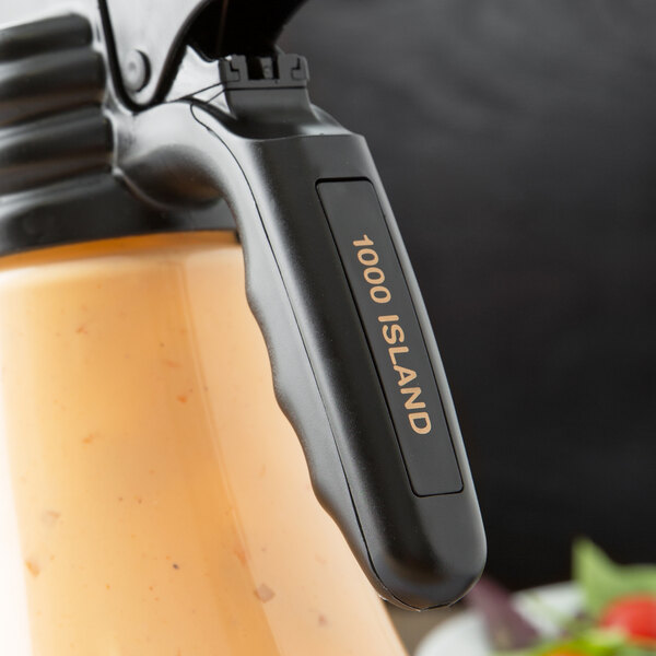 A Tablecraft black polypropylene salad dressing dispenser tag with orange print and a black handle.