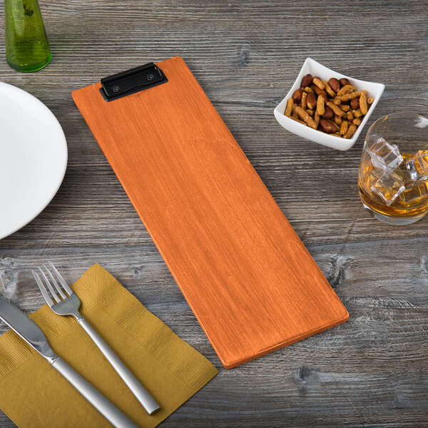 A wooden clipboard holding a menu next to a plate and a bowl of nuts.