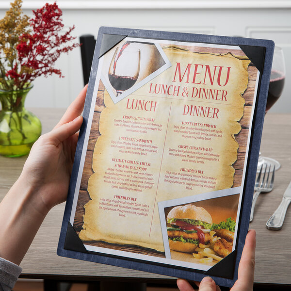 A hand holding a Menu Solutions wood menu board with a picture corner on a table with a fork and knife.