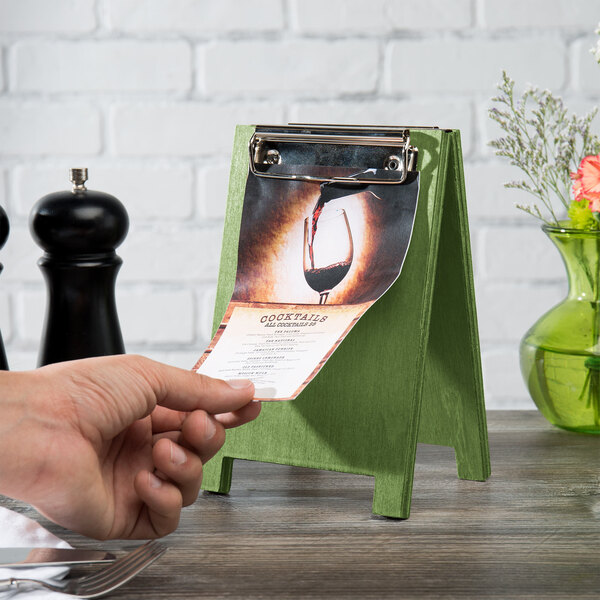 A hand using a Menu Solutions lime wood menu board tent with clip on a table.