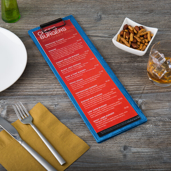 A blue wooden menu clip board holding a red menu, placed on a table setting with utensils, a plate, a drink, and a bowl of snacks.