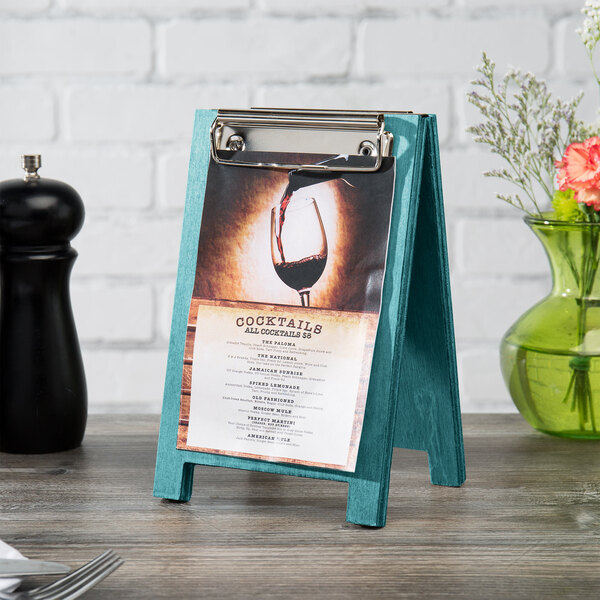 A sky blue wood Menu Solutions sandwich menu board tent with a clip on a table with a menu.