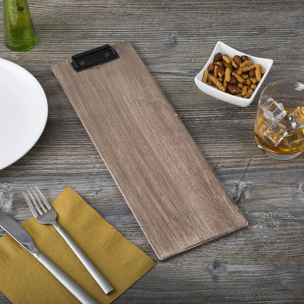 A weathered walnut wood clipboard holding a menu next to a plate and bowl of nuts.