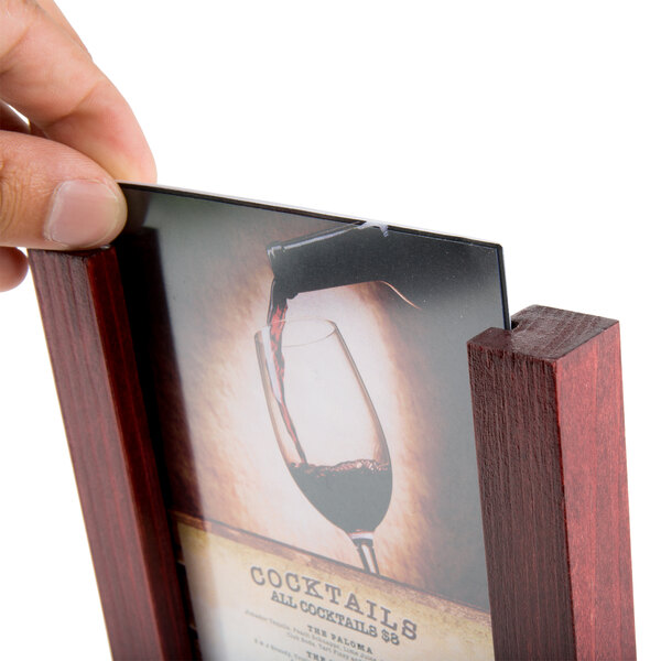A hand holding a Menu Solutions mahogany wood table tent with a 4" x 6" insert over a table with a glass of red wine.