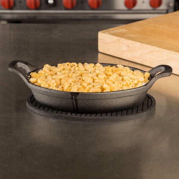 Cast iron casserole dish filled with macaroni and cheese with cutting board in background