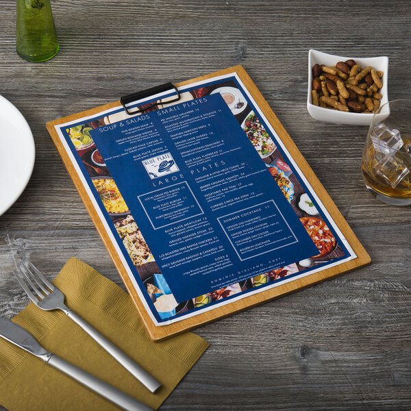 A Menu Solutions Country Oak wood menu clip board on a table with a fork and knife on a napkin.
