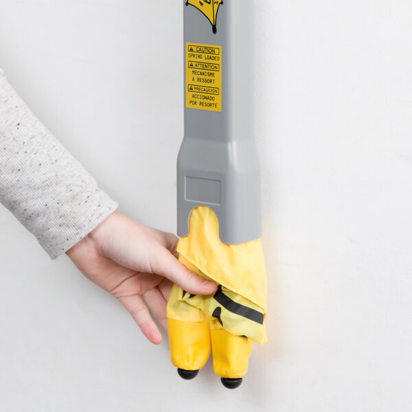 A hand wearing a yellow glove holding a yellow and black Rubbermaid wet floor sign.