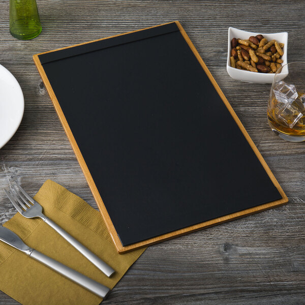 A customizable wood menu board with top and bottom strips on a table with a bowl of nuts and a glass of liquid.