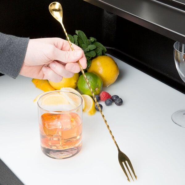 A hand using a Barfly gold plated fork to garnish a cocktail with a lime.