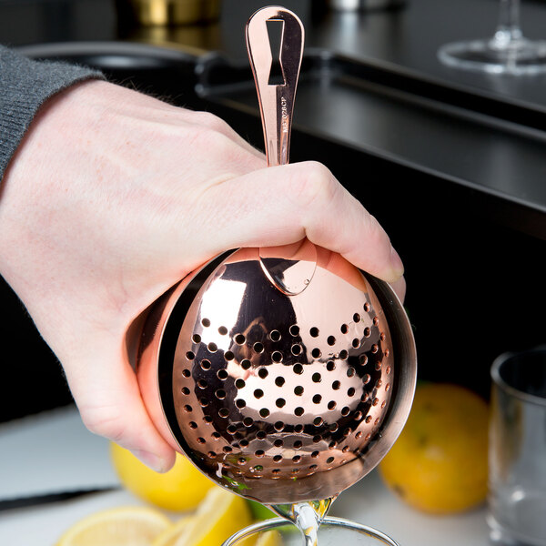 A person using a Barfly copper-plated Julep strainer to pour a drink.
