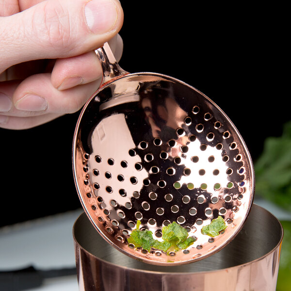 A person using a Barfly copper julep strainer over a cup.
