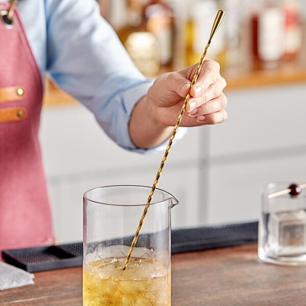 A woman using a Barfly gold plated double end stirrer in a cocktail.