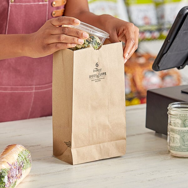 A woman holding a Duro brown paper bag full of food at a register.