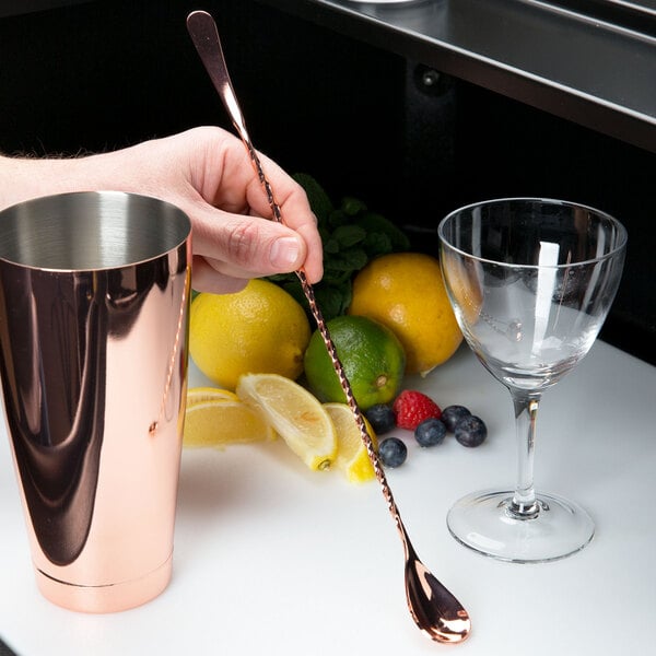 A hand using a Barfly copper plated Japanese style bar spoon to stir a drink.