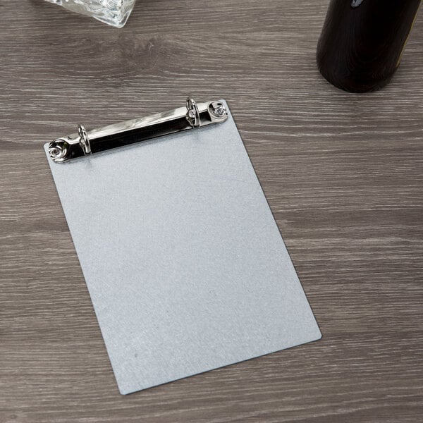 A Menu Solutions aluminum clipboard with metal rings on a wood table.