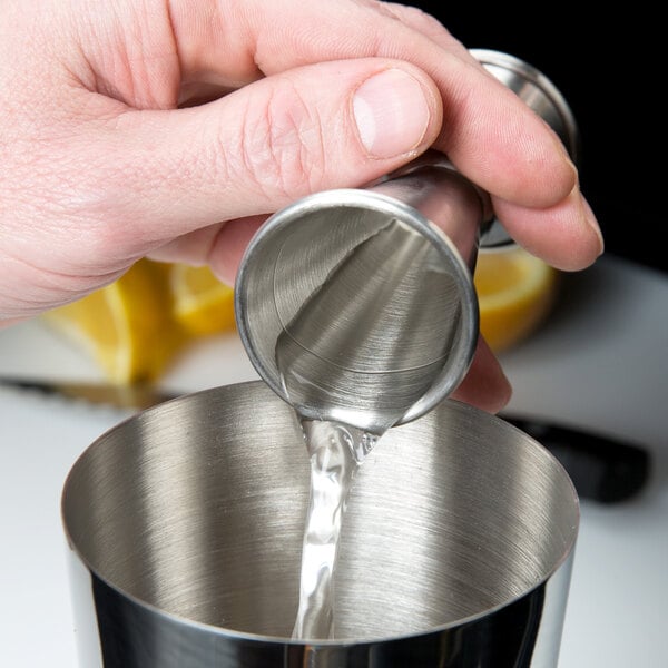 A person using a Barfly stainless steel Japanese jigger to pour liquid into a metal cup.