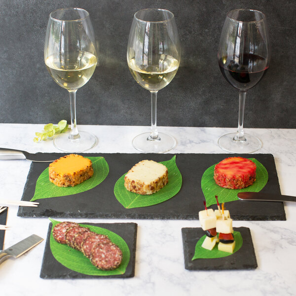 A rectangular black slate tray with food and four glasses of wine on a table.