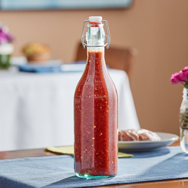 An Arcoroc tinted green glass bottle of red sauce sits on a table in a Mexican restaurant.