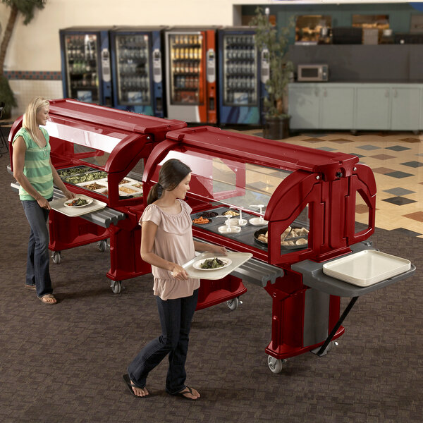 Two women using a Cambro hot red Versa salad bar in a hospital cafeteria.